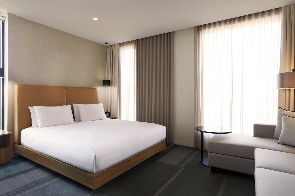 A hotel room with a large bed, a sofa, a small table, and a wall-mounted lamp.