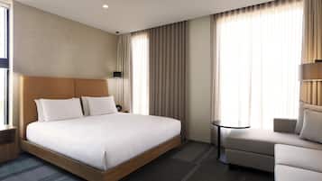 A hotel room with a large bed, a sofa, a small table, and a wall-mounted lamp.