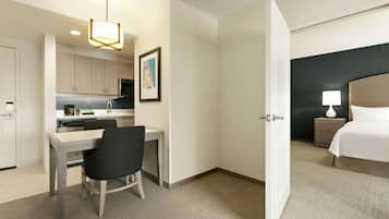 A hotel room with a bed, bedside table, lamp, and a view of the kitchen area.