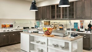 Een moderne keuken met donkere houten kastjes, een centraal eiland met een fruitschaal, en een koffiehoek.