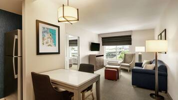 A modern hotel room with a dining area, a sofa, a TV, and a large window.
