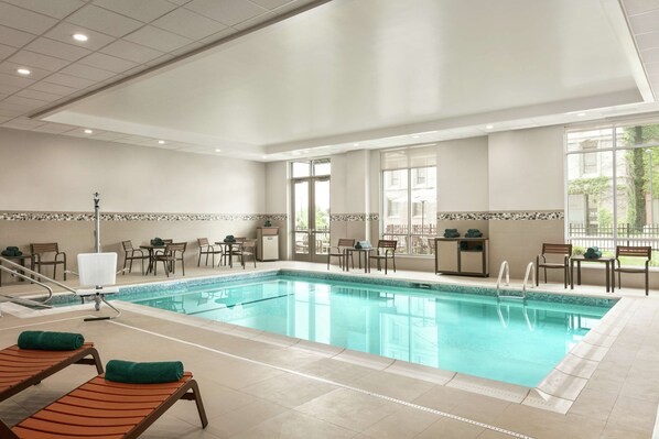 Une grande piscine intérieure dotée de nombreux fauteuils et tables, et entourée de baies vitrées offrant une vue sur l’extérieur.