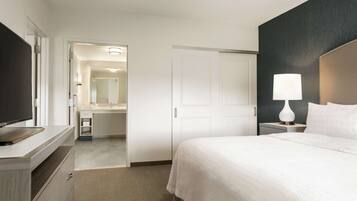 A hotel room with a bed, a TV, a desk, and a bathroom visible through an open door.
