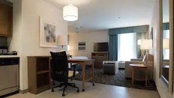 Een hotelkamer met een kitchenette, een zithoek met een tafel en stoelen, een bank, een televisie en een groot raam met gordijnen.