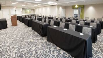 Un salón de conferencias con mesas dispuestas en filas, un atril y una alfombra estampada.