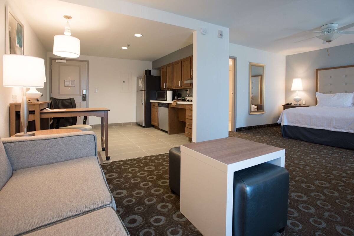 A hotel room with a bed, a desk, a kitchenette, and a seating area.