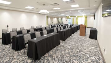 A conference room with rows of tables and chairs, a podium, and a patterned carpet.