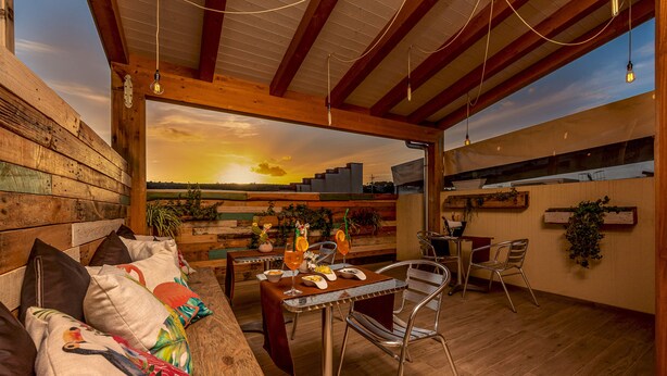 A wooden deck with a dining table and chairs, a cushioned bench, and a view of the sunset. - Ayres Del Mar (San Vito Lo Capo)