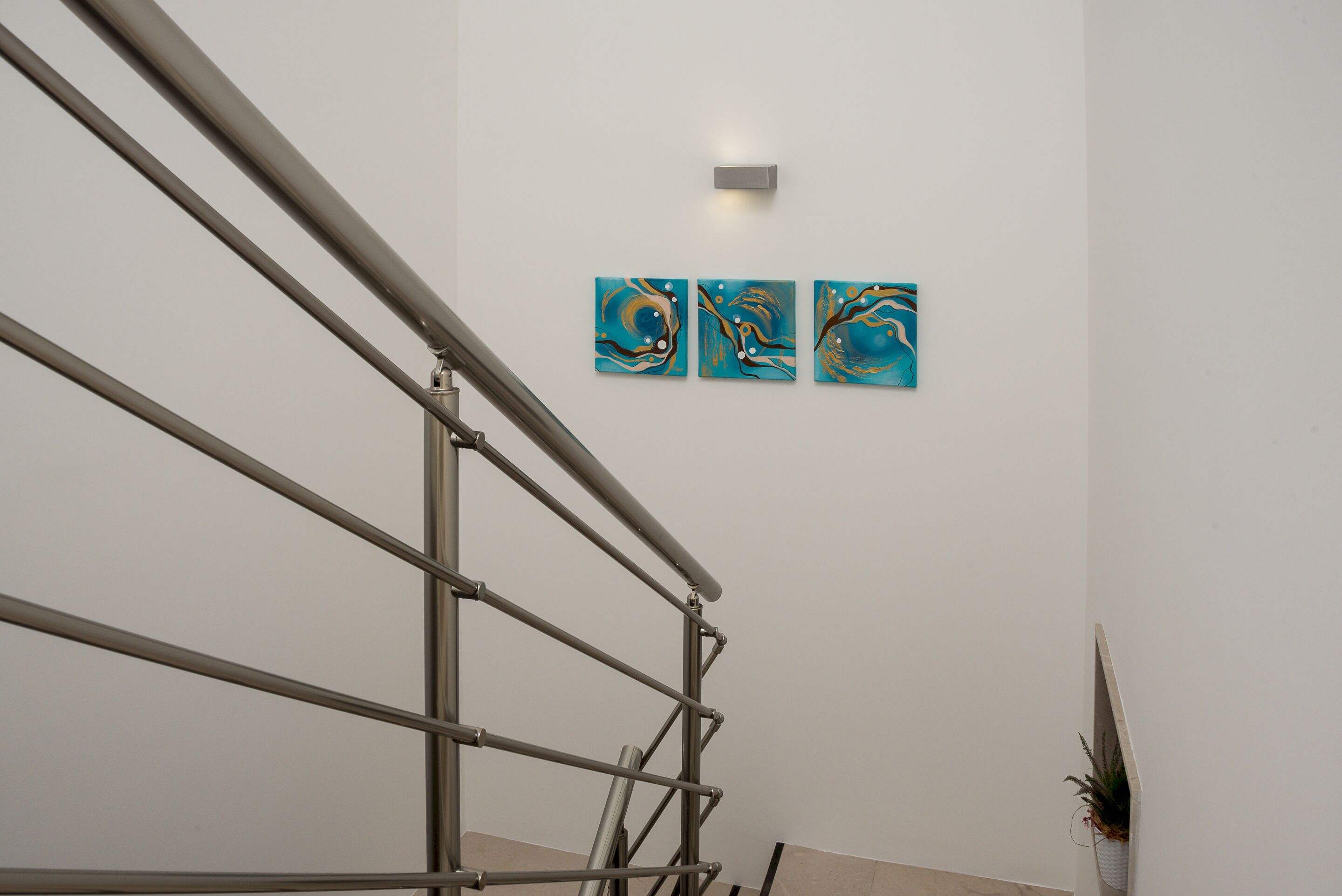 A staircase with metal railings leading to a landing. There are three abstract paintings on the wall above the staircase.