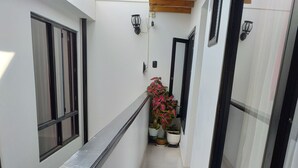 Un pasillo estrecho con paredes blancas, ventanas de marco negro y suelo de baldosas.