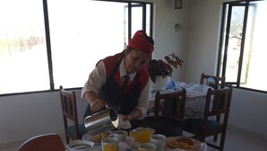 Un comedor con una mesa preparada para el desayuno, que incluye platos de comida, tazas y una persona sirviendo una bebida.