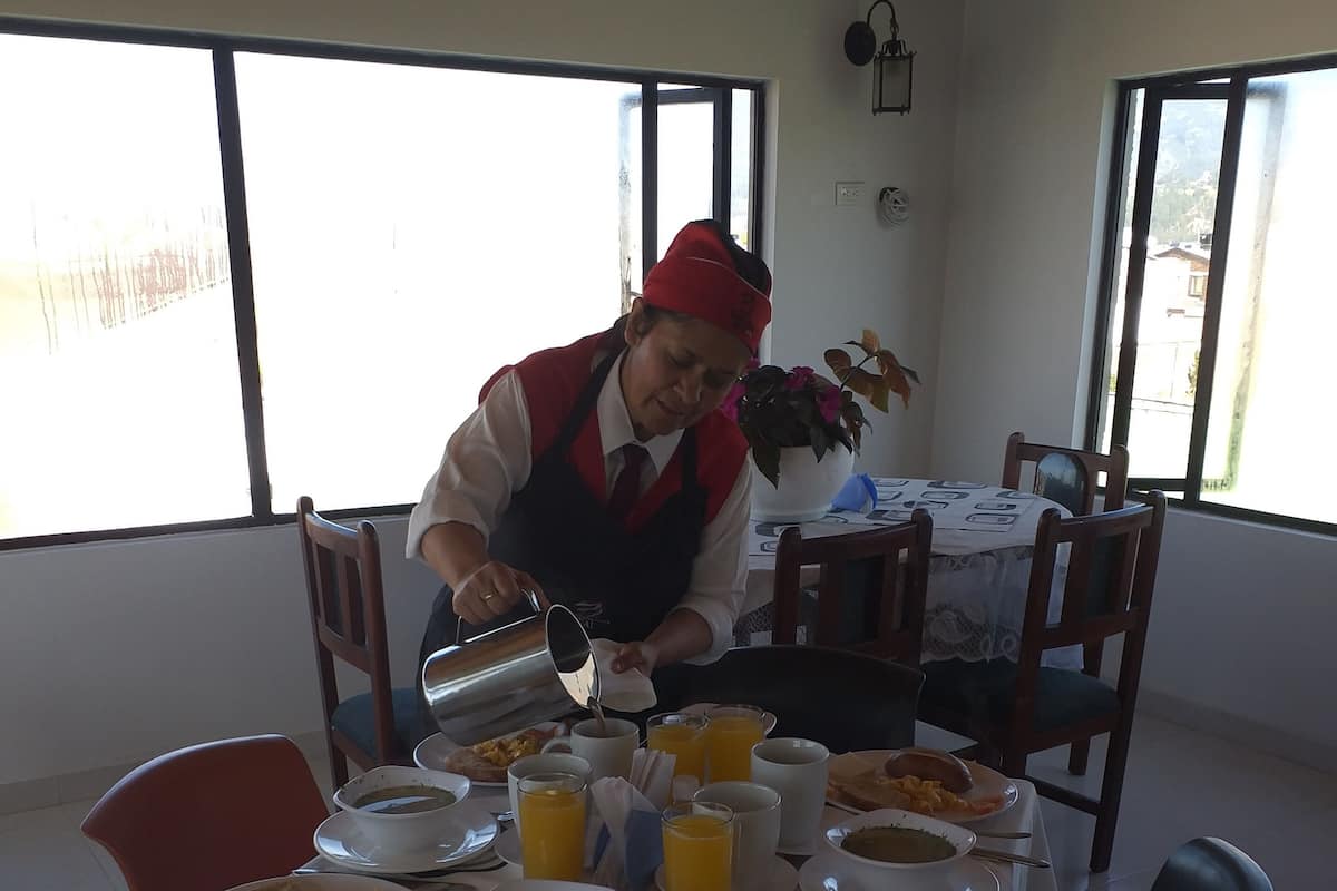 Uma área de refeições com uma mesa posta para o café da manhã, incluindo pratos de comida, xícaras e uma pessoa servindo uma bebida.