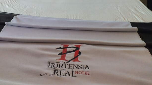 Una cama bien tendida con sábanas y almohadas blancas, un cabecero negro y una manta blanca doblada con un logotipo y texto.