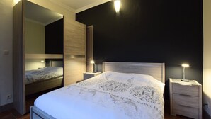 Un dormitorio con cama, mesitas de noche, un espejo e iluminación en la pared.