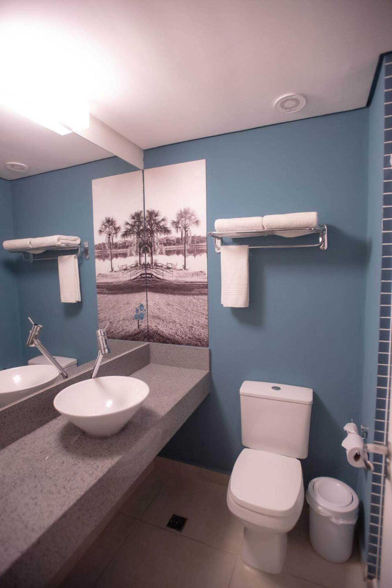 Et badeværelse med blå væg, hvid vask, toilet og håndklædestang.