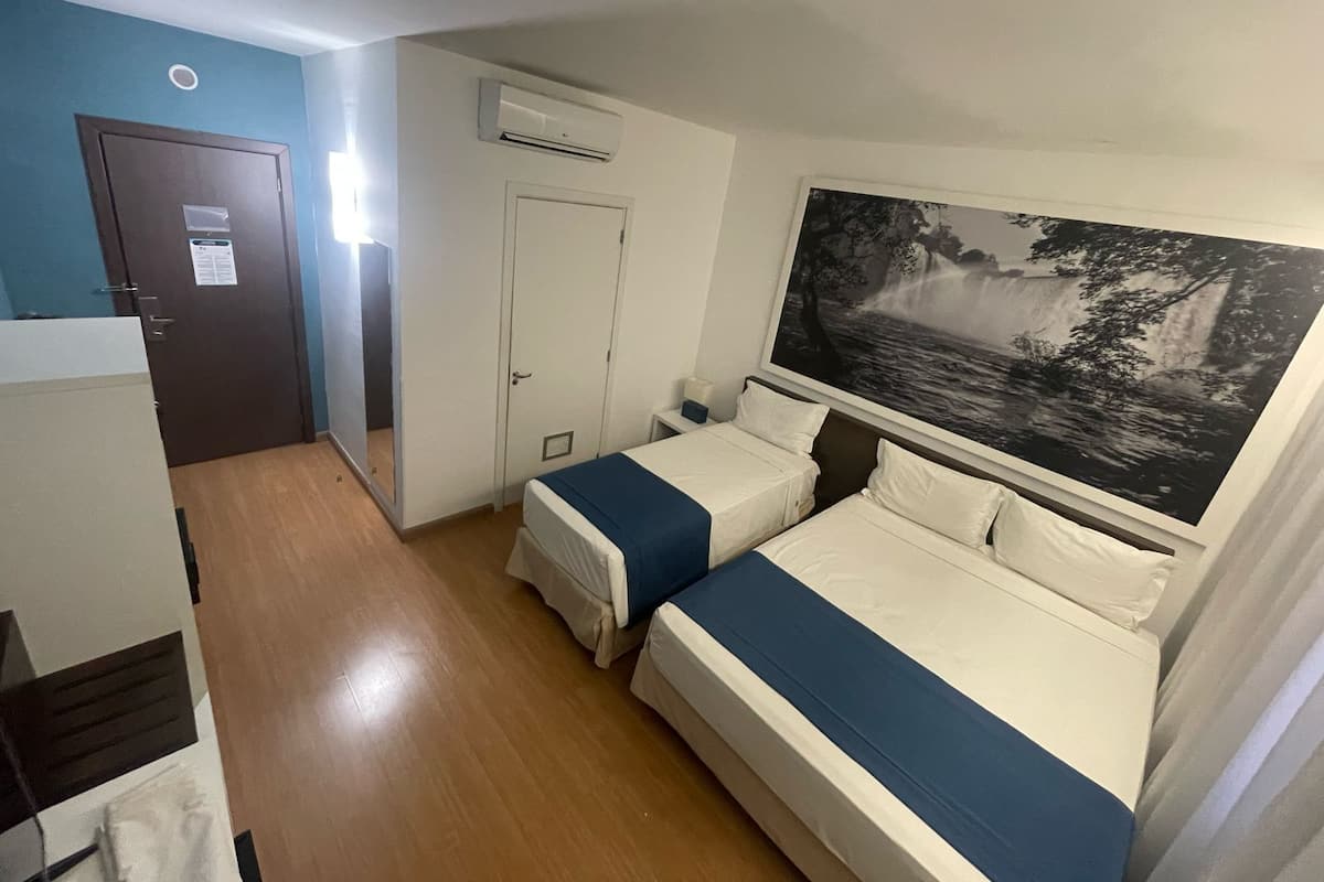 A hotel room with two beds, a wardrobe, an air conditioning unit, and a large framed picture on the wall.