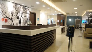 A hotel reception area with a modern reception desk, a check-in counter, and a seating area with a television. - Golden Tower Aeroporto - Lizz - By Fênix Hotéis (Uberlandia)