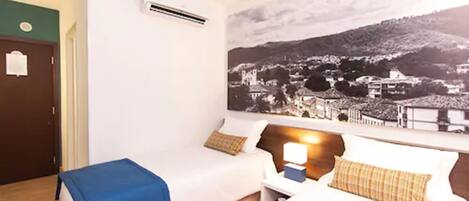 A hotel room with a bed, a chair, a nightstand, and a wall-mounted air conditioner.