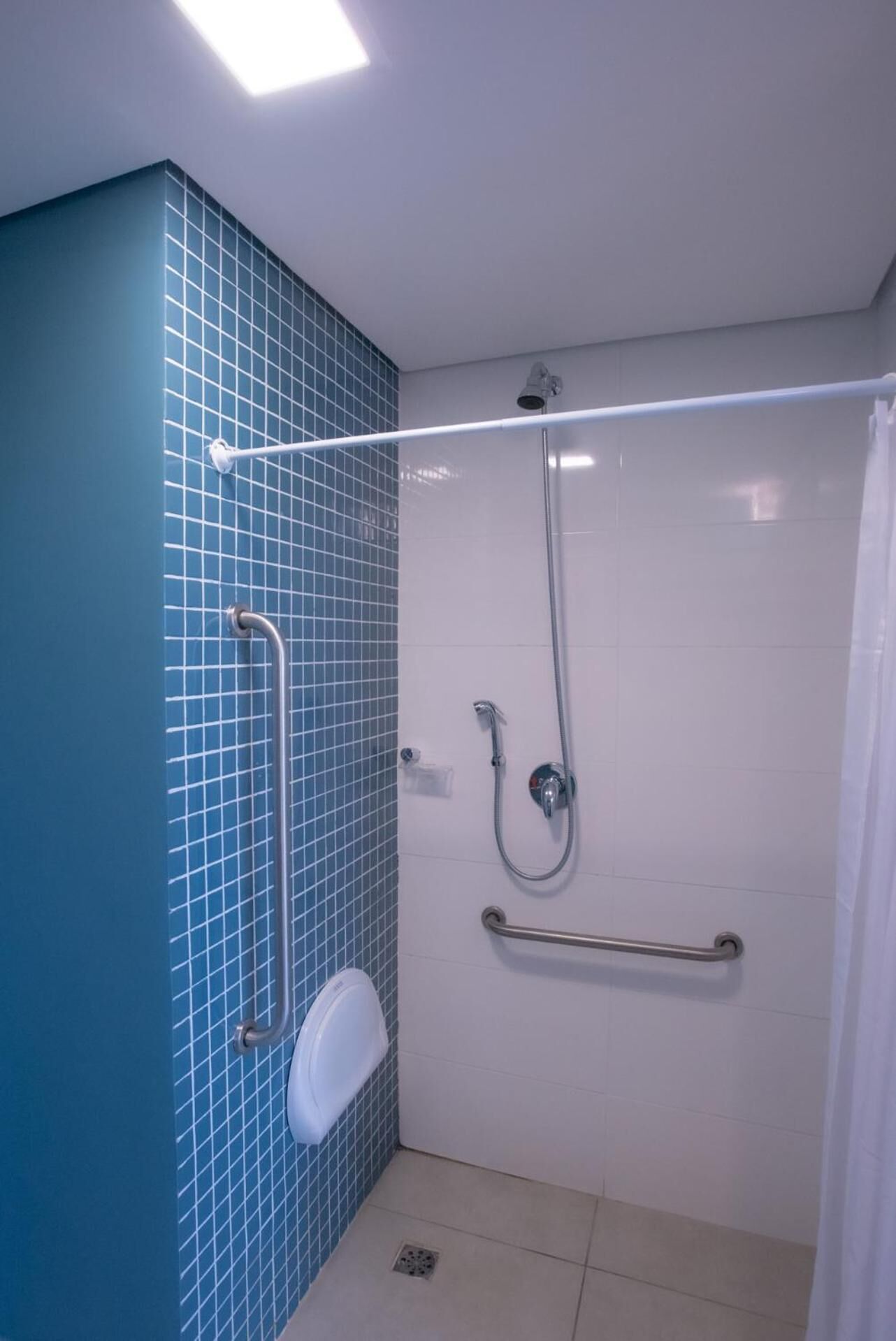Un baño moderno con pared de azulejos azules, inodoro blanco, ducha de mano y barra de apoyo.