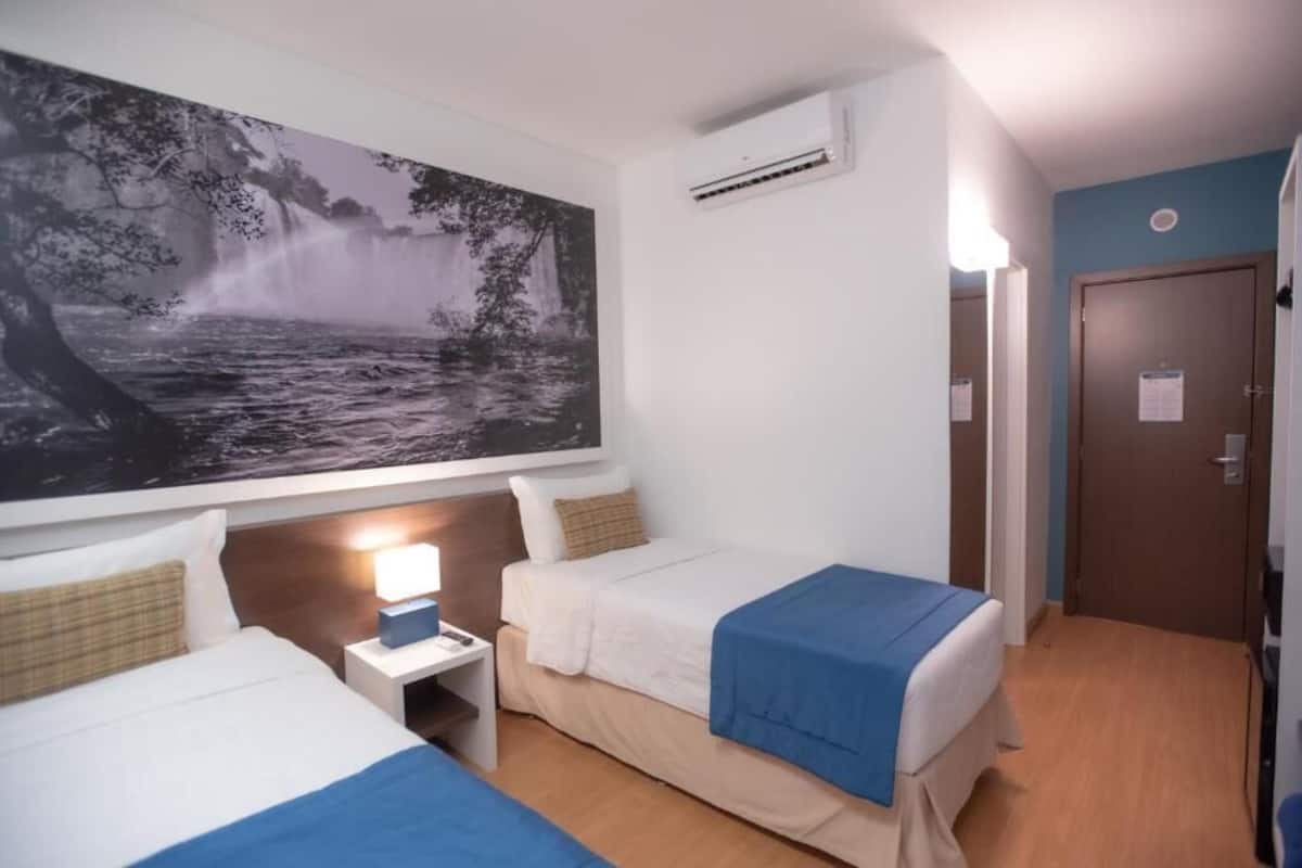 A hotel room with two beds, a nightstand, a wall-mounted air conditioner, and a door with a notice.