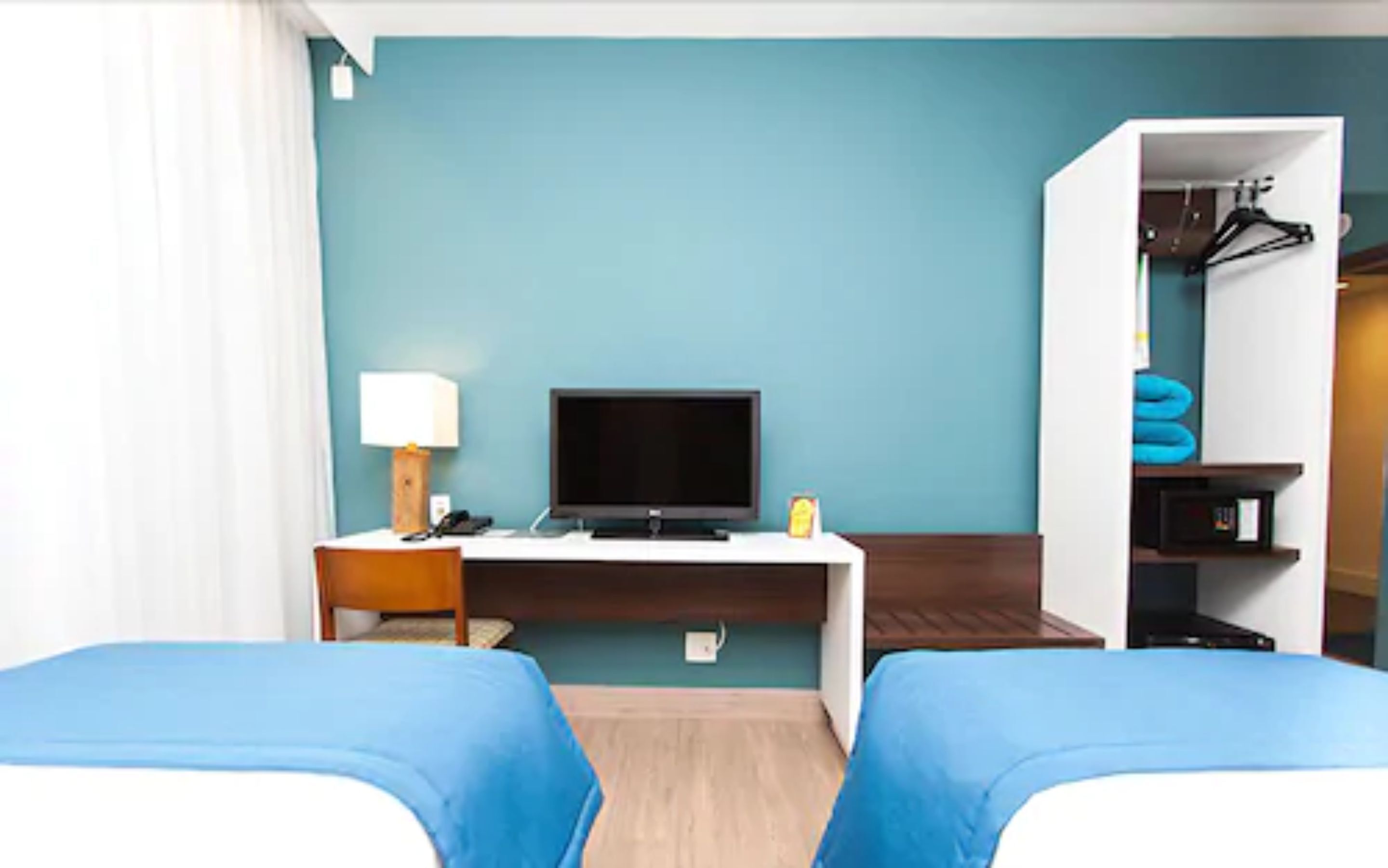 Une chambre d’hôtel avec deux lits, un bureau avec une télévision, une lampe et une armoire.