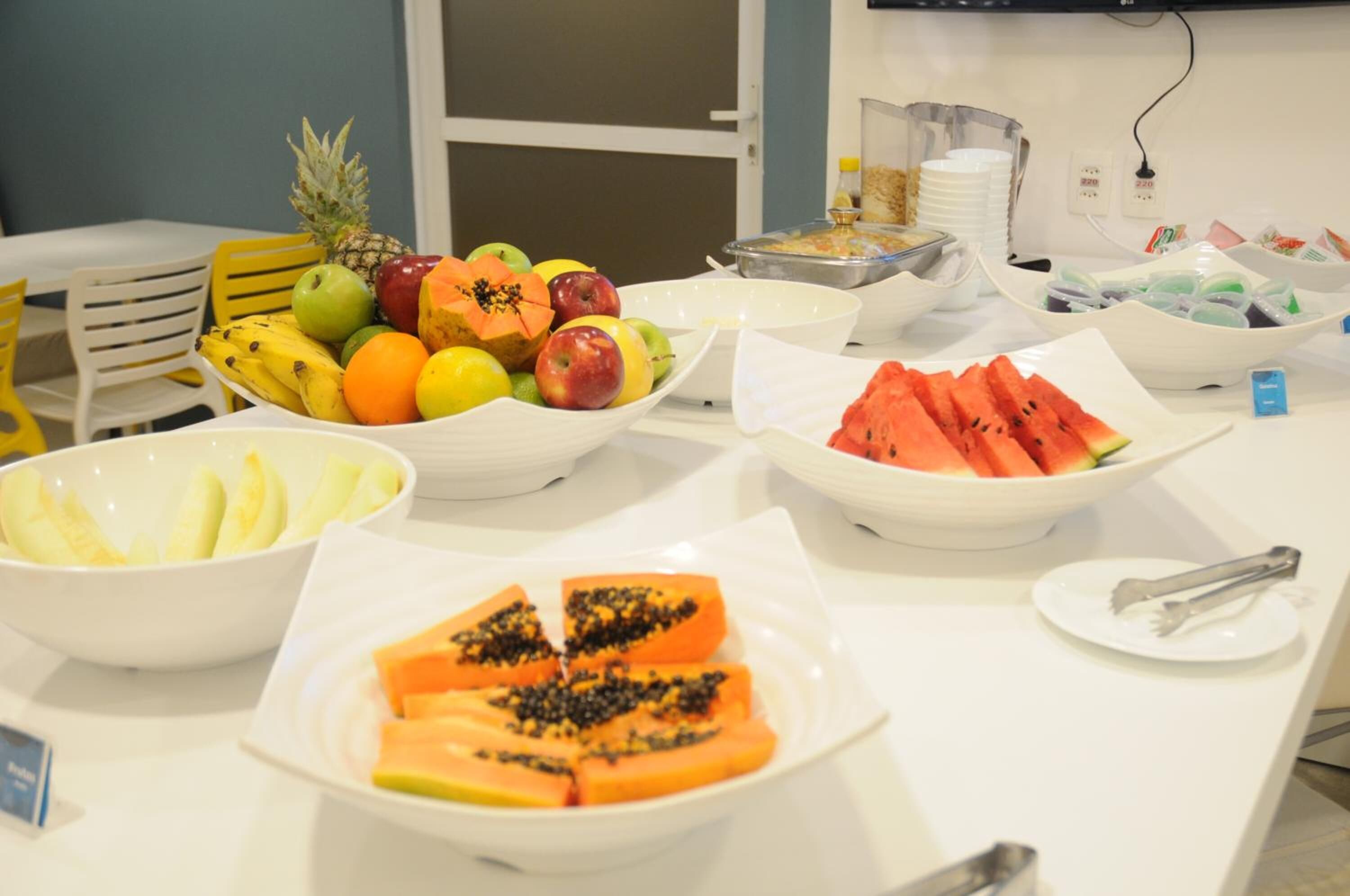 A buffet table with various fruits and a bowl of sliced watermelon.