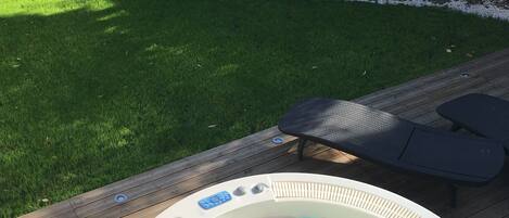 A hot tub on a wooden deck with a grassy yard in the background.