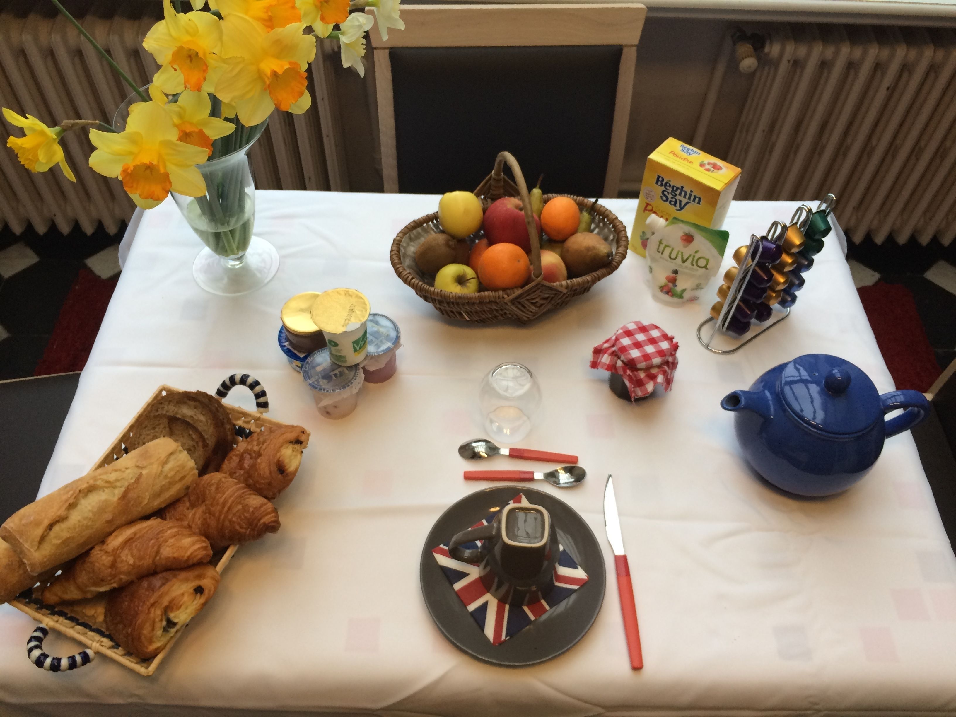 A breakfast table with croissants, a fruit basket, a teapot, and a jug of milk.
