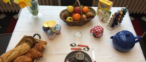 A breakfast table with croissants, a fruit basket, a teapot, and a jug of milk.