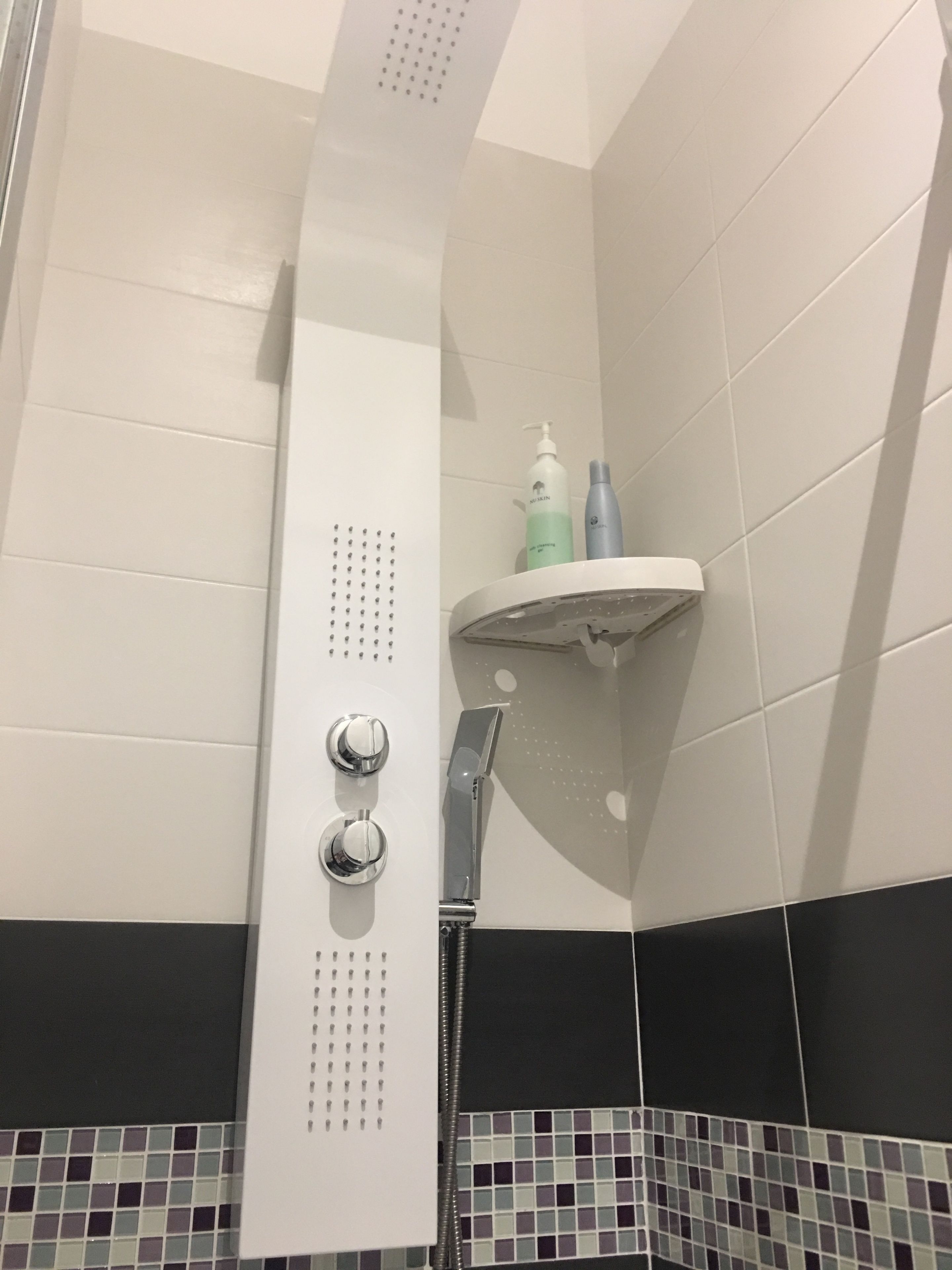 Un área de ducha con pared blanca, parte inferior negra y estante con artículos de aseo.