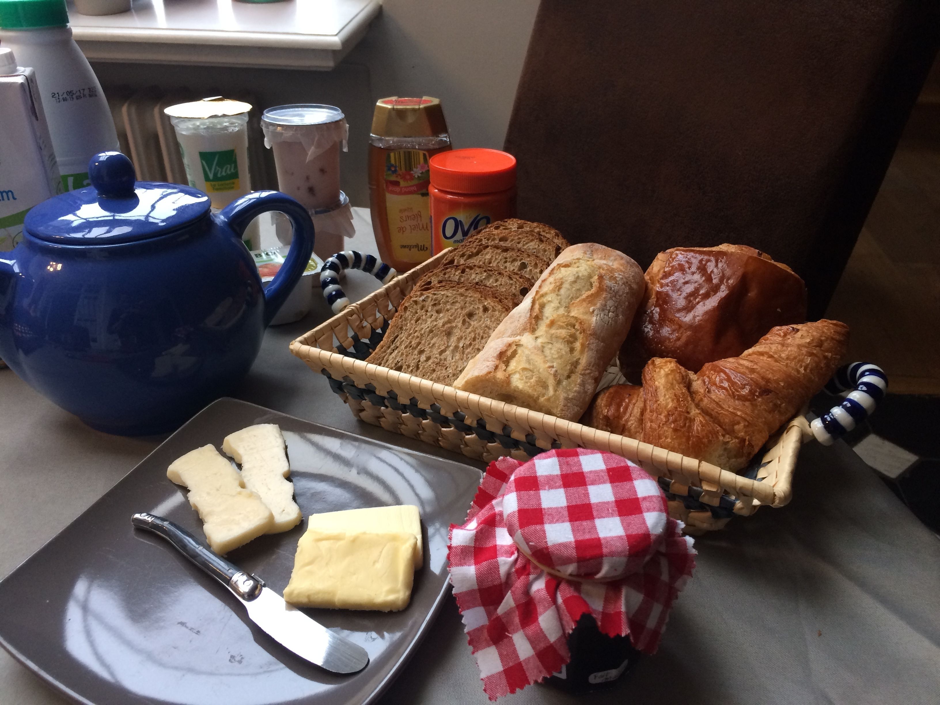 Una mesa con pan, croissants, mantequilla y una tetera para el desayuno.
