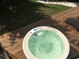 Un jacuzzi en una terraza de madera, con un área verde de fondo.
