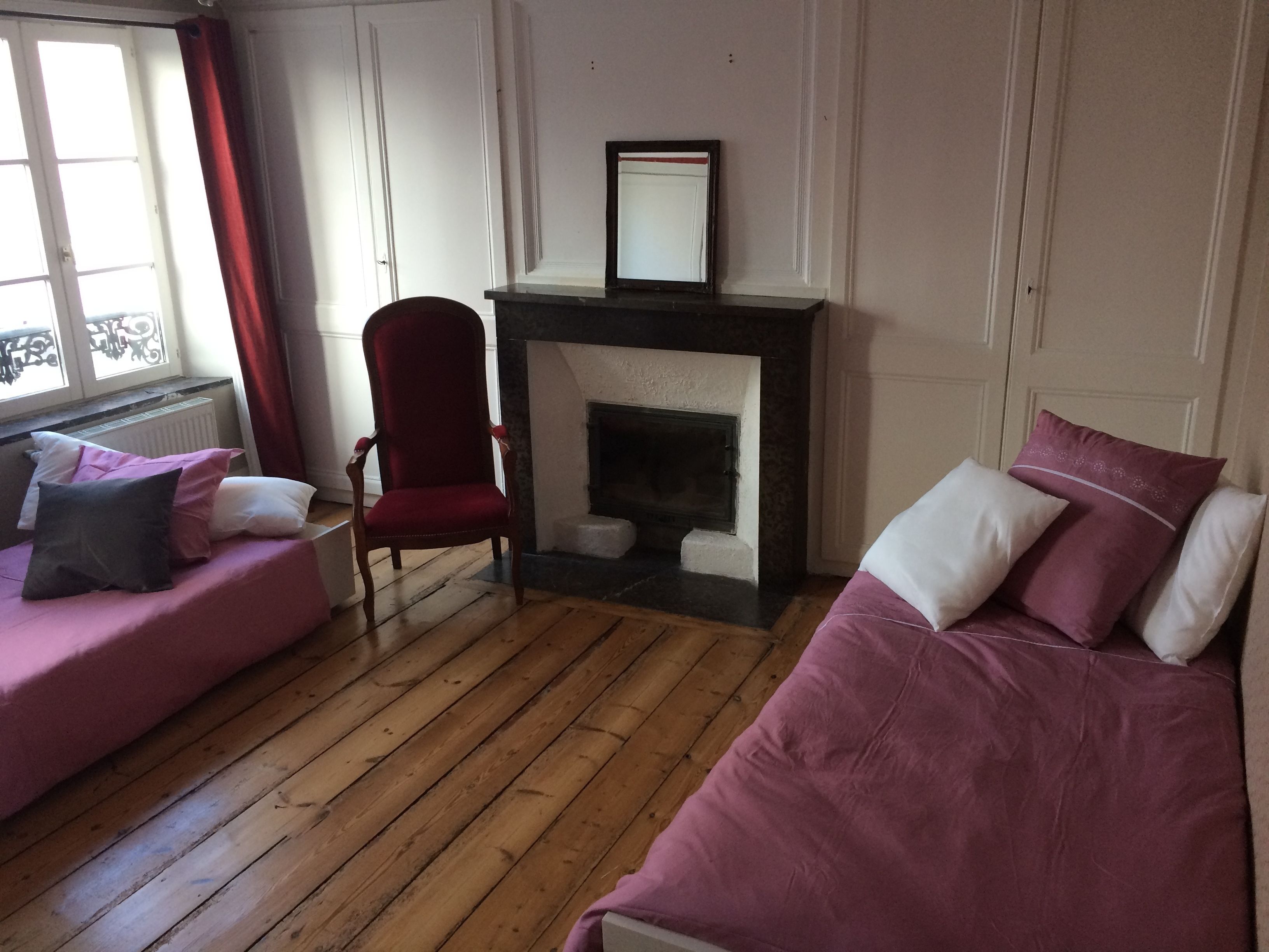 A room with a fireplace, two pink sofas, a red armchair, and a window with curtains.
