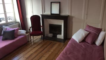 A room with a fireplace, two pink sofas, a red armchair, and a window with curtains.
