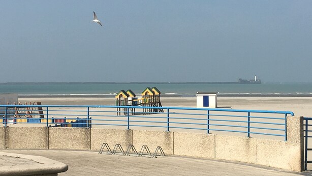 Une promenade en bord de mer, agrémentée d’une barrière en béton, de rampes bleues et d’une rangée de cabanes de plage.