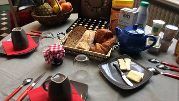A breakfast setup with bread, pastries, a coffee pot, and various condiments on a table.