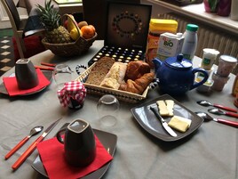 Una mesa con desayuno: pan, pasteles, una cafetera y diferentes condimentos.