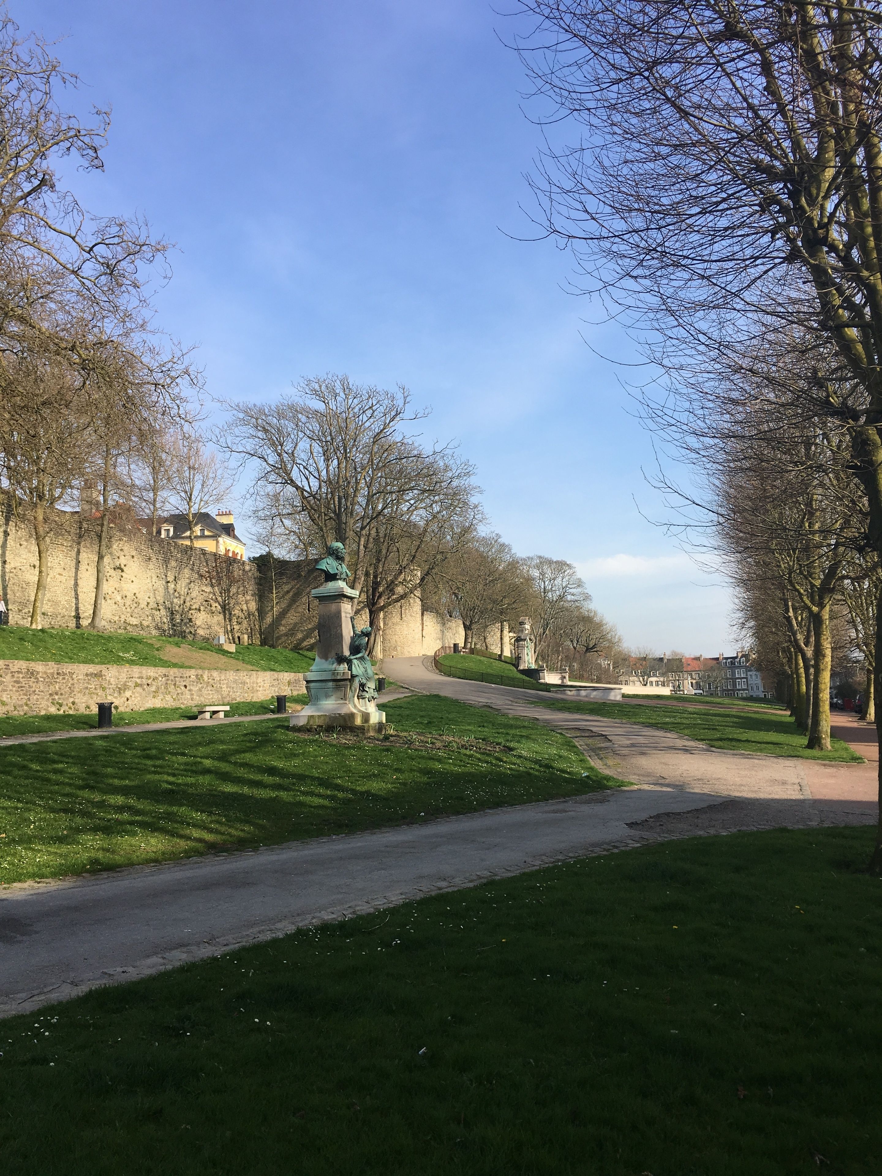 A park with a statue, a stone wall, and a pathway.