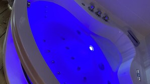 Un bain à remous moderne, de forme ovale, doté d’un éclairage bleu, d’un panneau de commande et d’un sol en bois qui l’entoure.