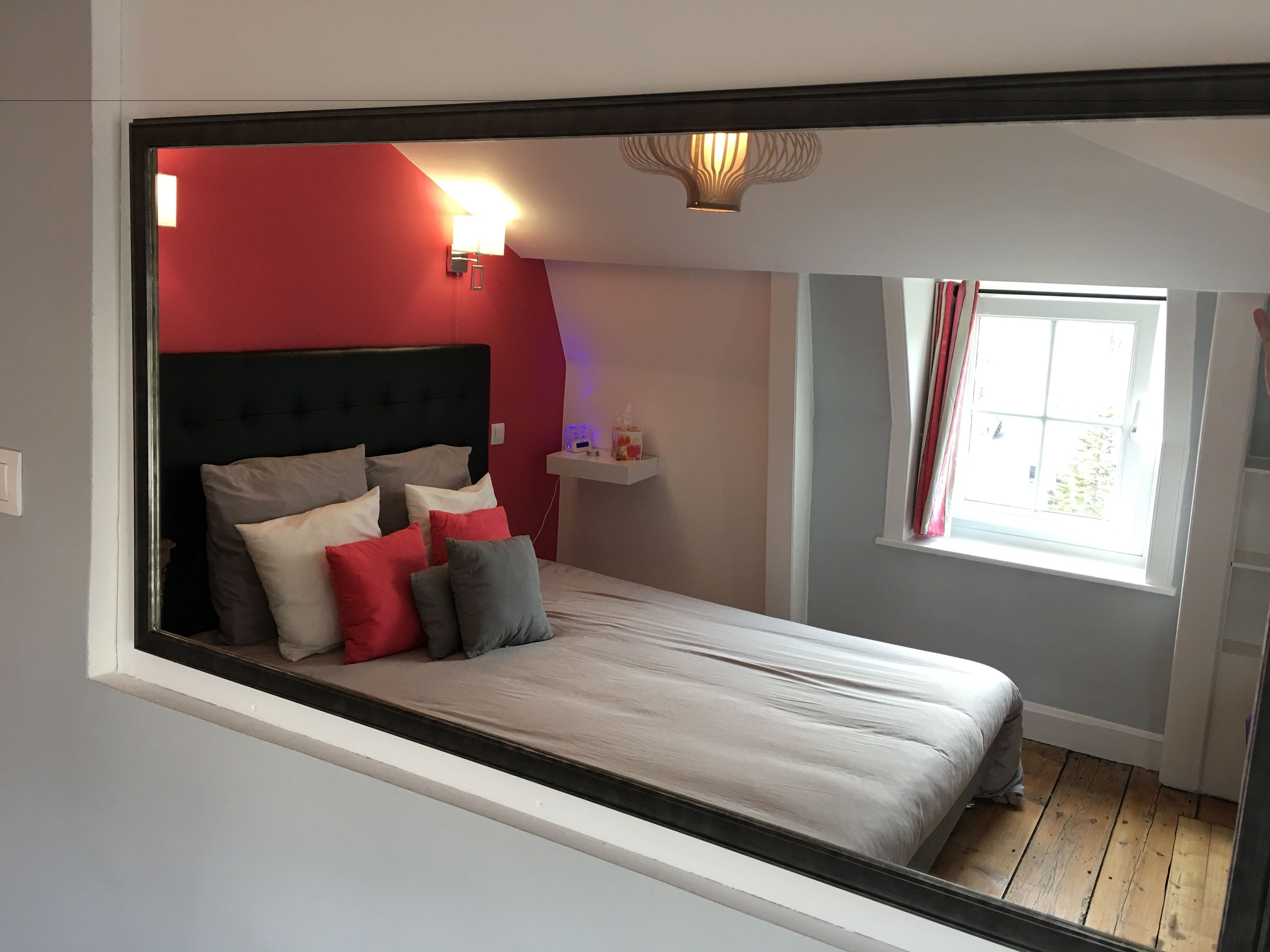 A bedroom with a bed, red walls, a window, and a nightstand.