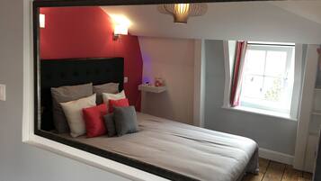 A bedroom with a bed, red walls, a window, and a nightstand.