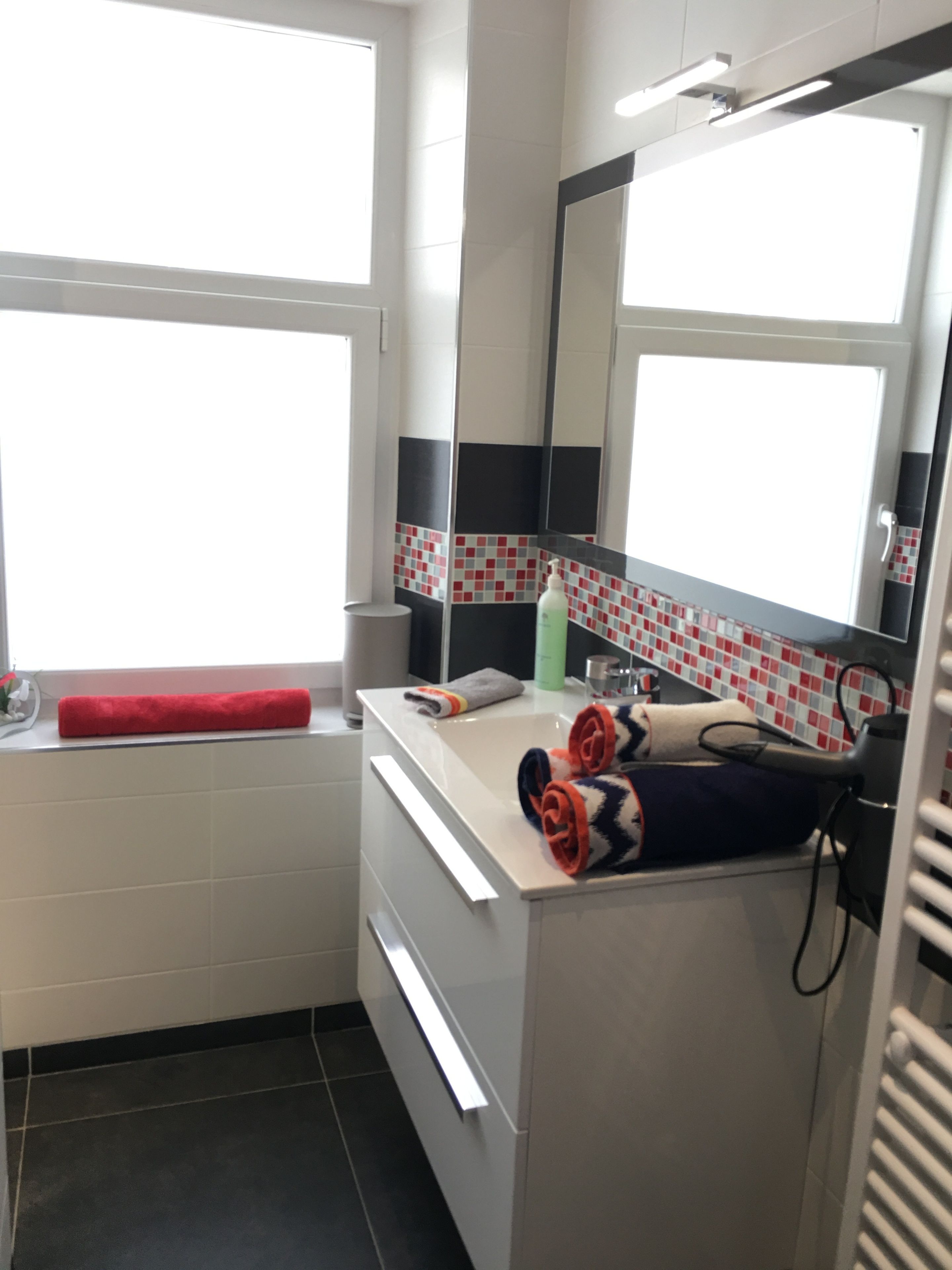 A bathroom with a window, a mirror, a sink, and towels.