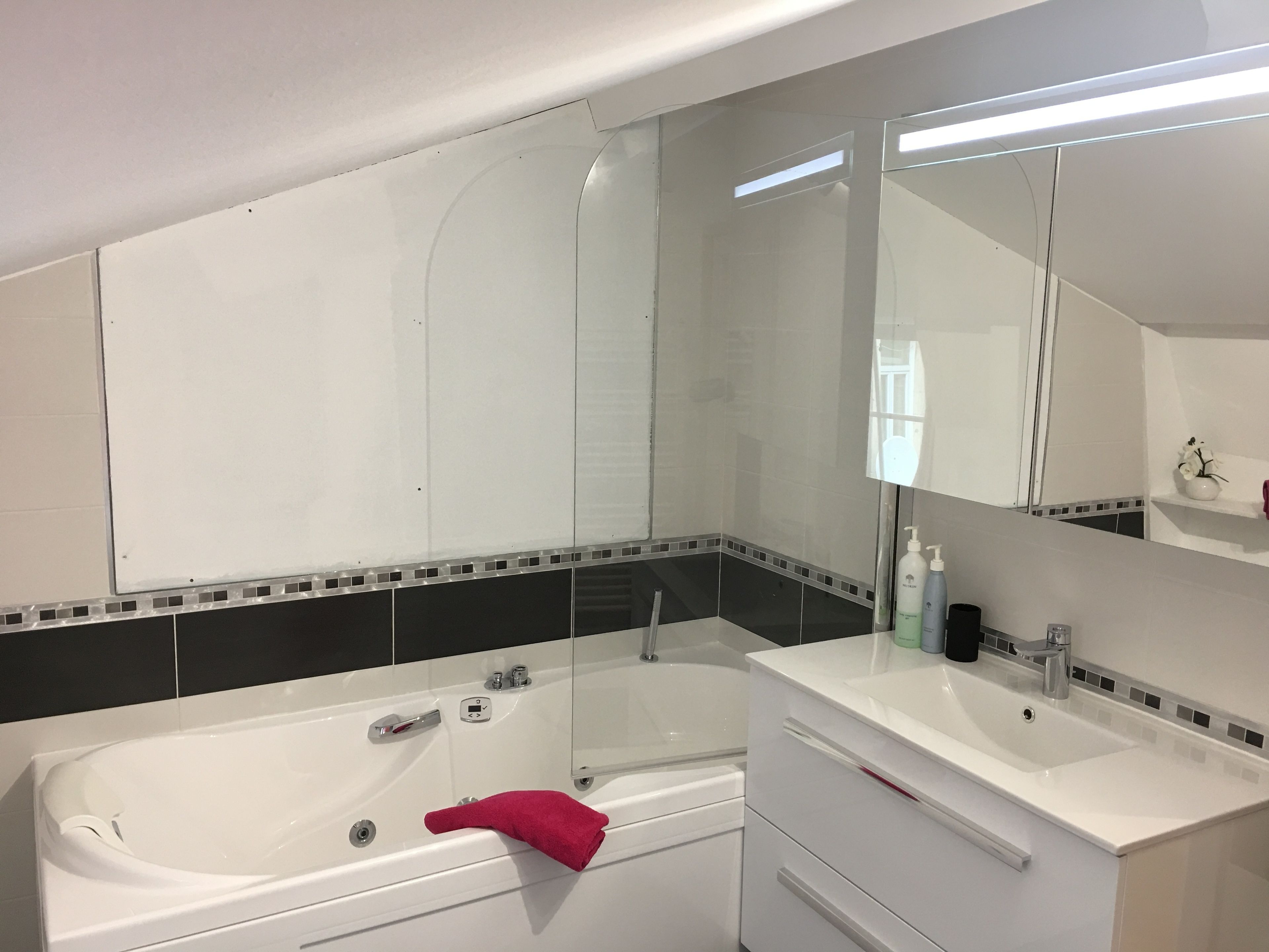 A modern bathroom with a bathtub, a large mirror, and a vanity with a sink.