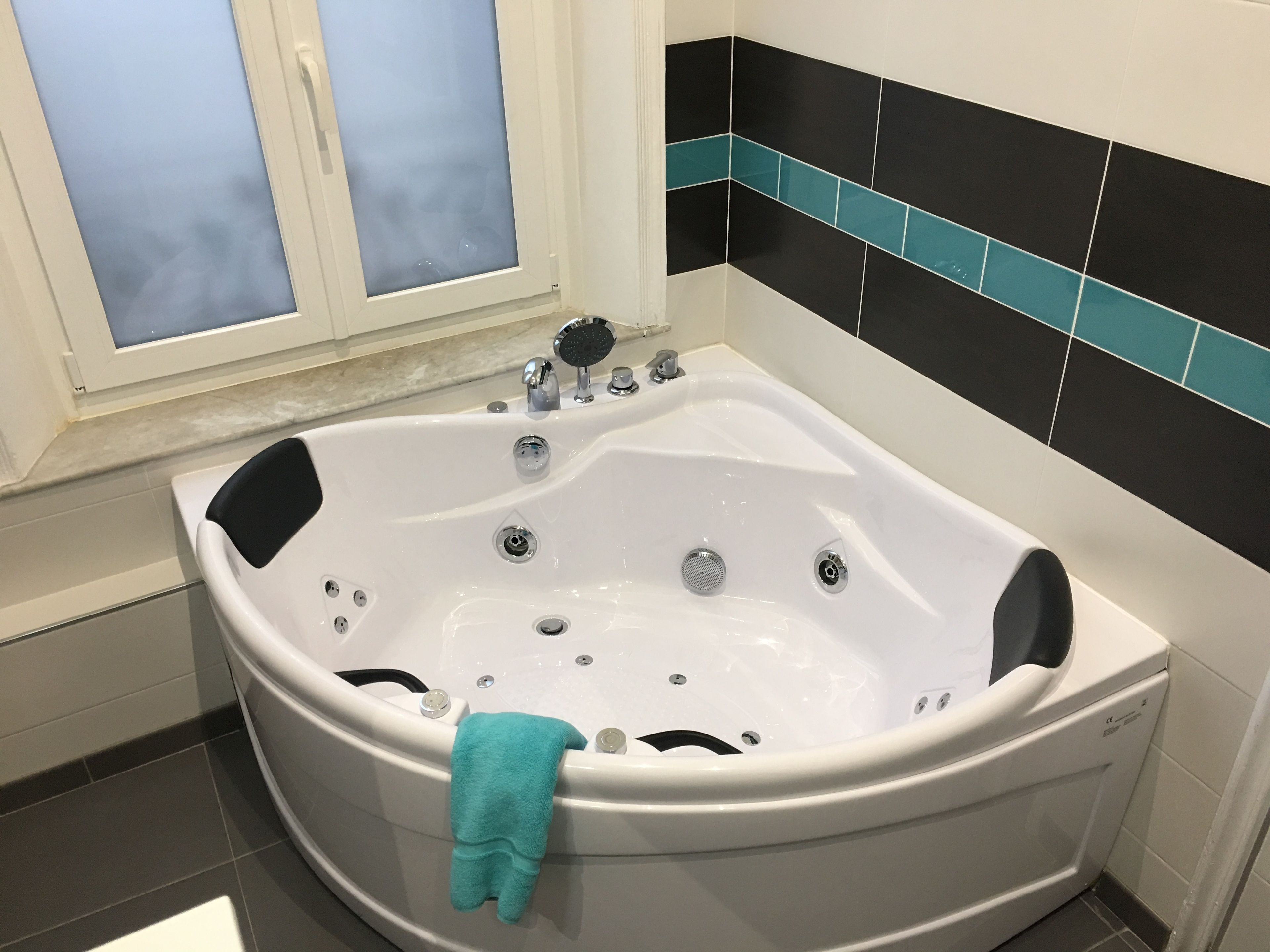 Un baño con una bañera independiente, un ventanal con vidrio esmerilado y paredes con azulejos blanco y negro.