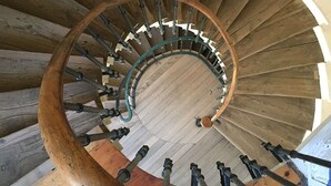 Un escalier en colimaçon en bois, doté d’une main courante en bois et de balustres en métal.