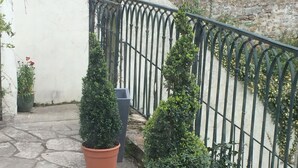 Un sentier pavé de pierres mène à une zone délimitée par une grille, où se trouvent des plantes en pot et une clôture métallique.