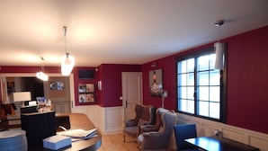 A modern living room with a wooden floor, a dining area with a table and chairs, a bar area with a counter and stools, and a large window providing natural light. - Contact Hôtel du Relais Thouars (Louzy)