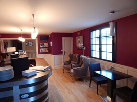 A modern living room with a wooden floor, a dining area with a table and chairs, a bar area with a counter and stools, and a large window providing natural light.