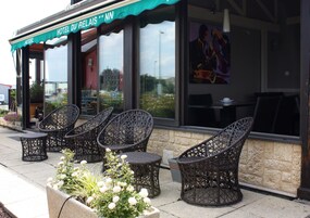 Outdoor wicker chairs and tables in front of a building with a sign reading "Hotel du Relais."