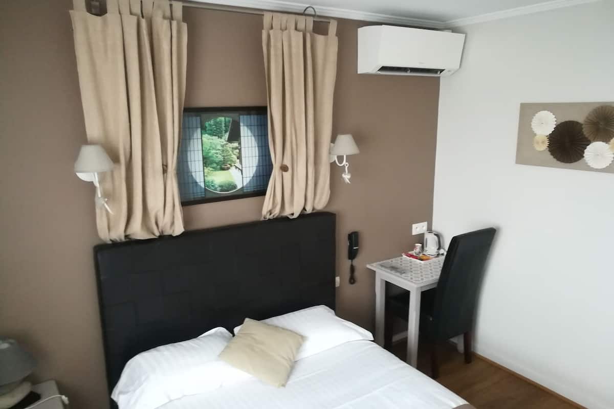 A hotel room with a bed, a desk, a chair, an air conditioner, a telephone, and a window with curtains.
